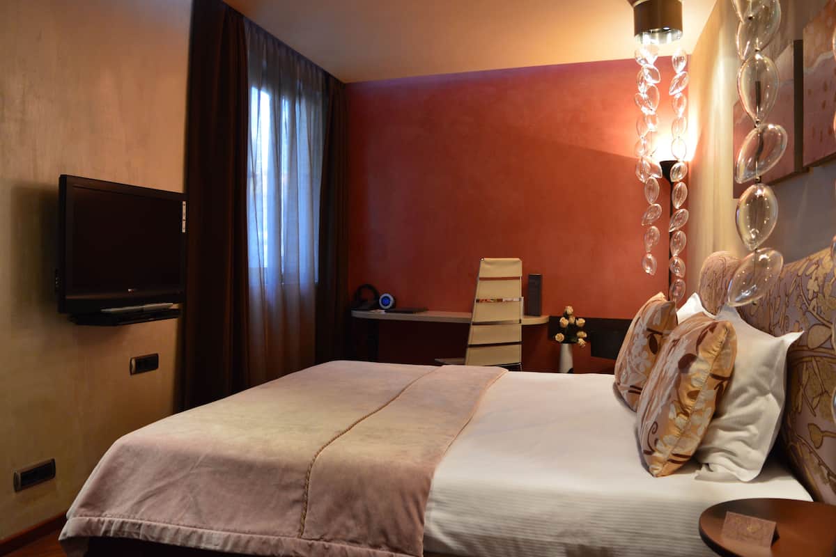 Una habitación de hotel con una cama, un televisor de pantalla plana montado en la pared, un escritorio con una silla y una lámpara decorativa.