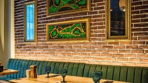 Un restaurante con pared de ladrillo, un banco acolchado verde, mesas de madera y vasos de vidrio verde.