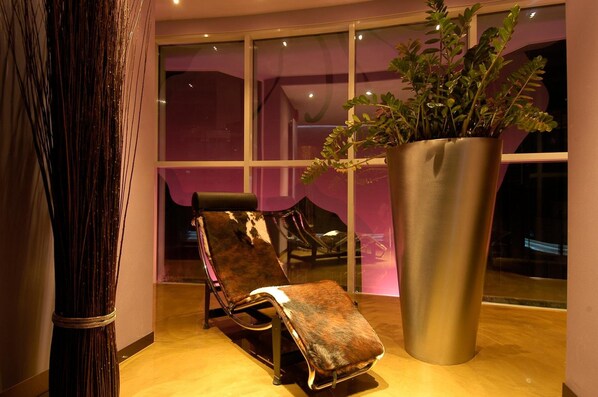 A modern lounge area with a leather chair, a large potted plant, and a glass partition.