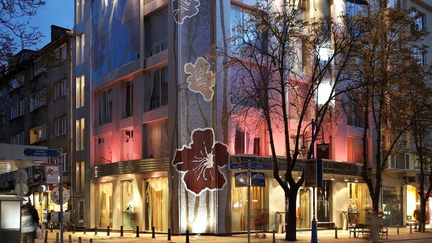Un edificio moderno con amplios ventanales y fachada curva, que presenta un llamativo diseño floral en el lateral.