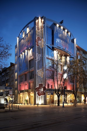 A modern building with large windows and a curved facade, featuring a prominent floral design on the side.