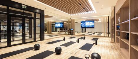 A modern fitness center with wooden flooring, black exercise mats, and exercise balls.