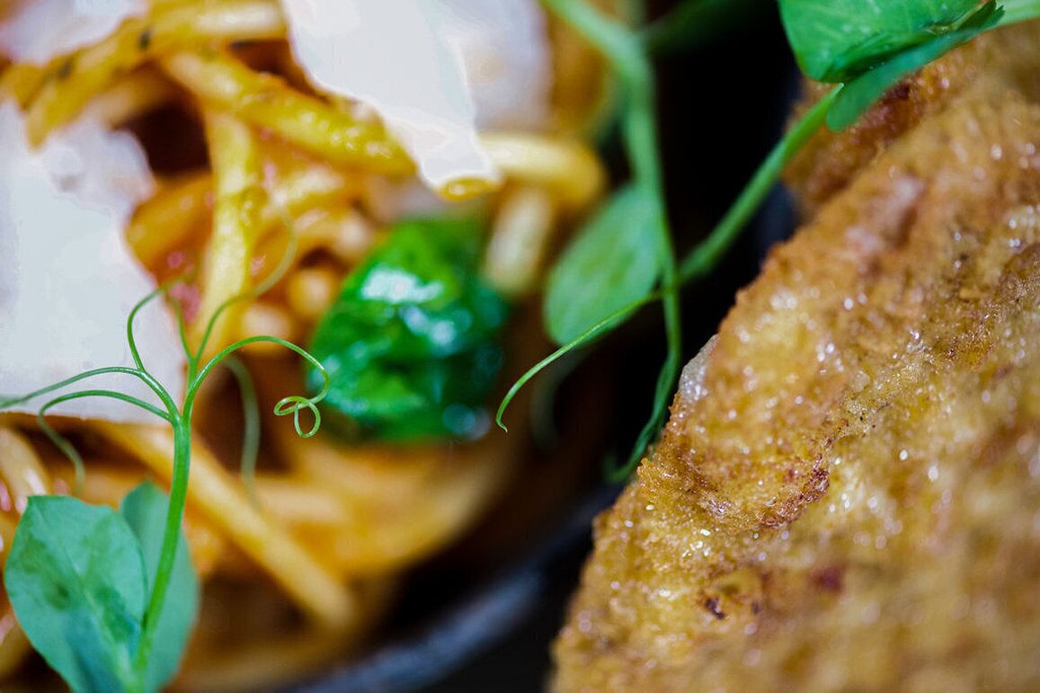 A close-up of a dish with pasta, greens, and a breaded item.