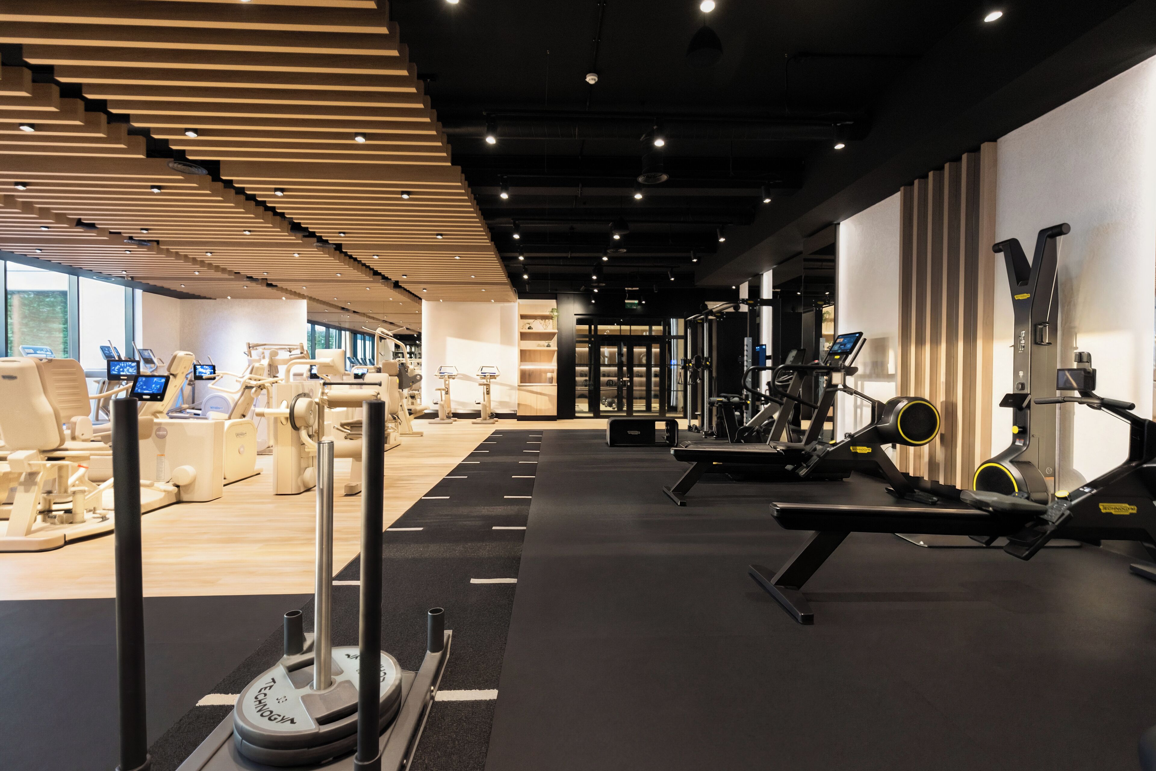 Un gimnasio moderno con diverso equipo de ejercicio, una zona de recepción y vistas de la ciudad a través de amplias ventanas.