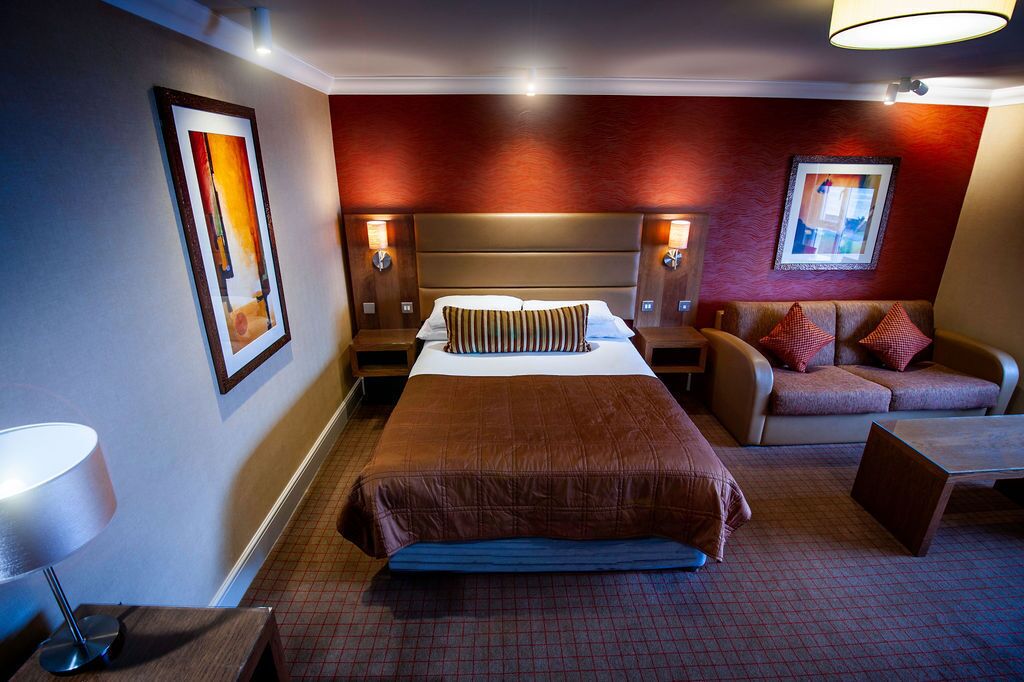 A hotel room with a large bed, a sofa, a desk, and two wall-mounted lamps.