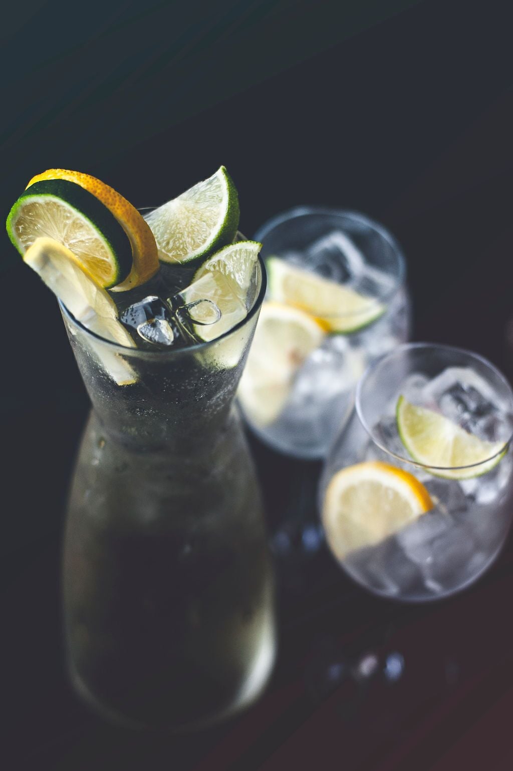 A glass of iced beverage with lime slices, accompanied by two smaller glasses with ice and lime slices.