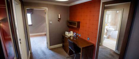 Habitación de hotel con un escritorio de madera, una silla, un espejo y un pequeño estante con artículos de aseo.