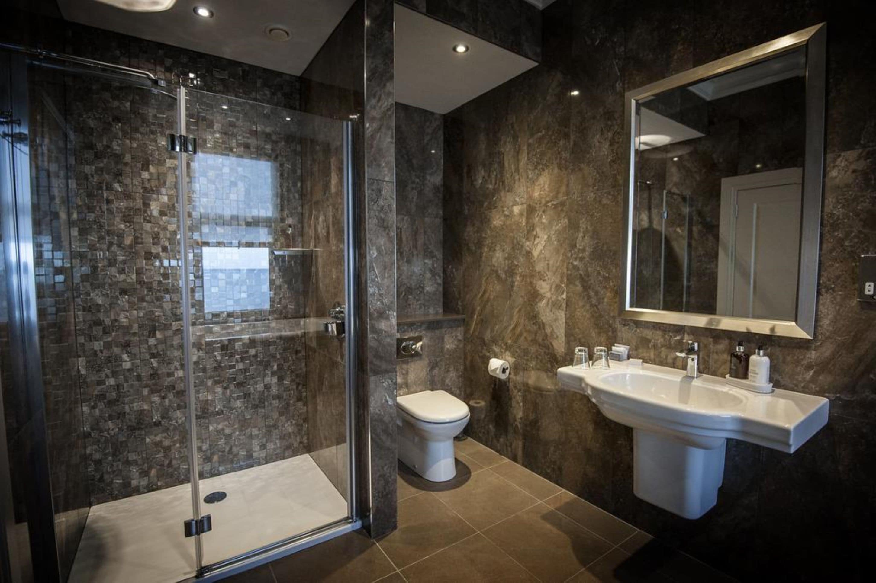 A modern bathroom with a glass shower enclosure, a white toilet, and a large sink with a mirror above it.