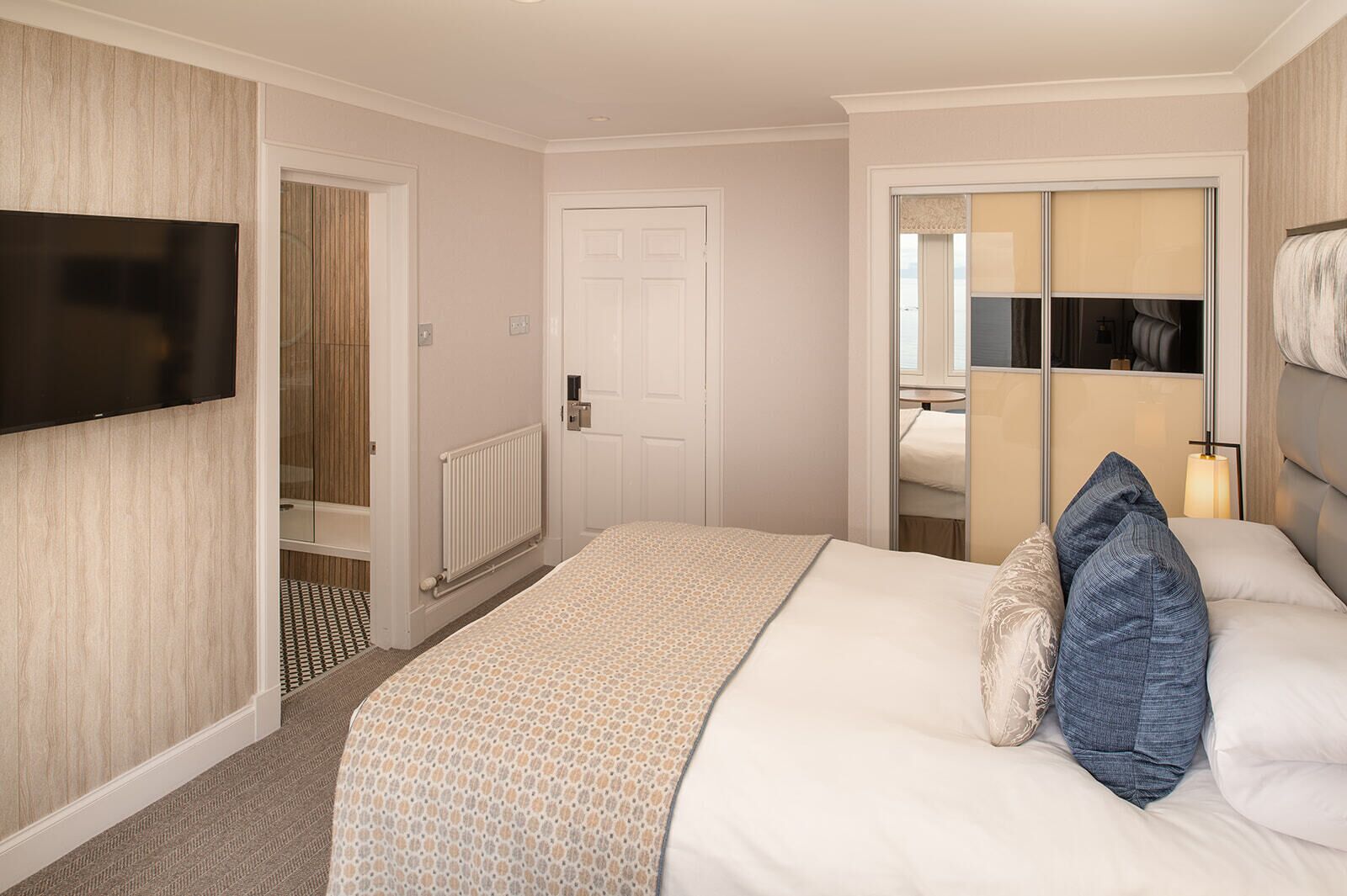 Habitación de hotel con una cama, televisión montada en la pared, puerta que da a un baño y una ventana con vistas.