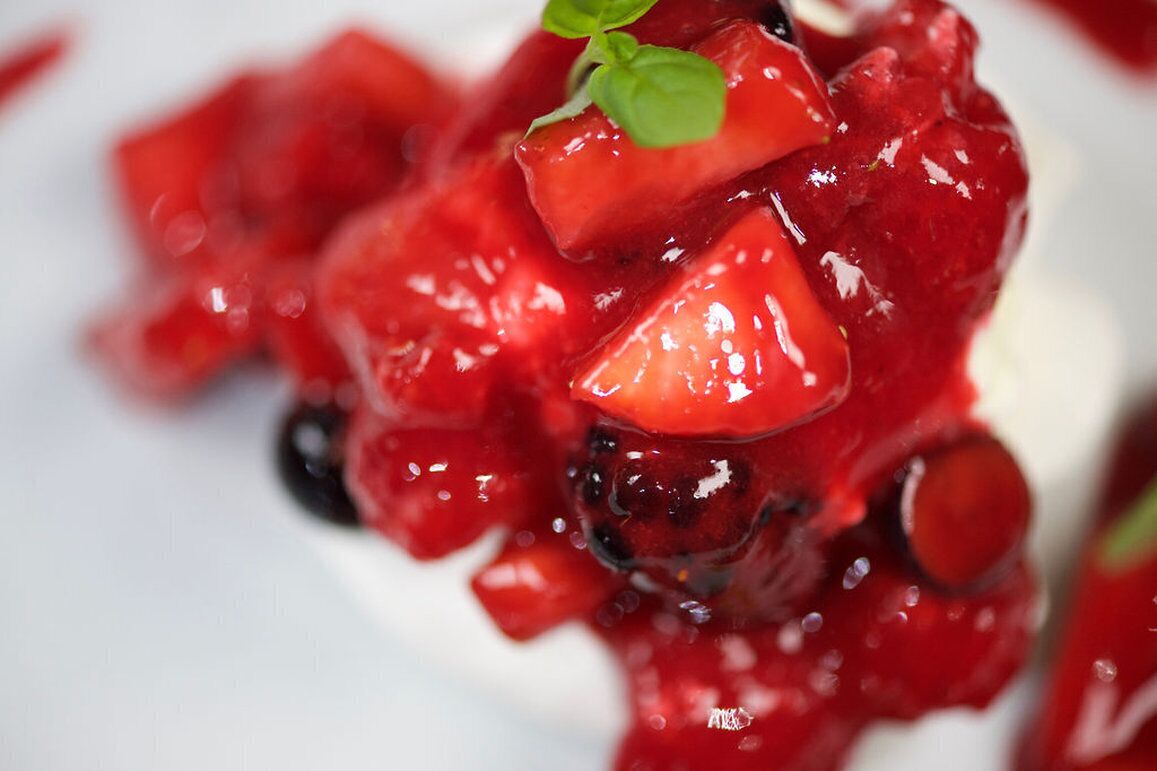 Gros plan d’un dessert aux fruits rouges, agrémenté d’une branche de menthe.