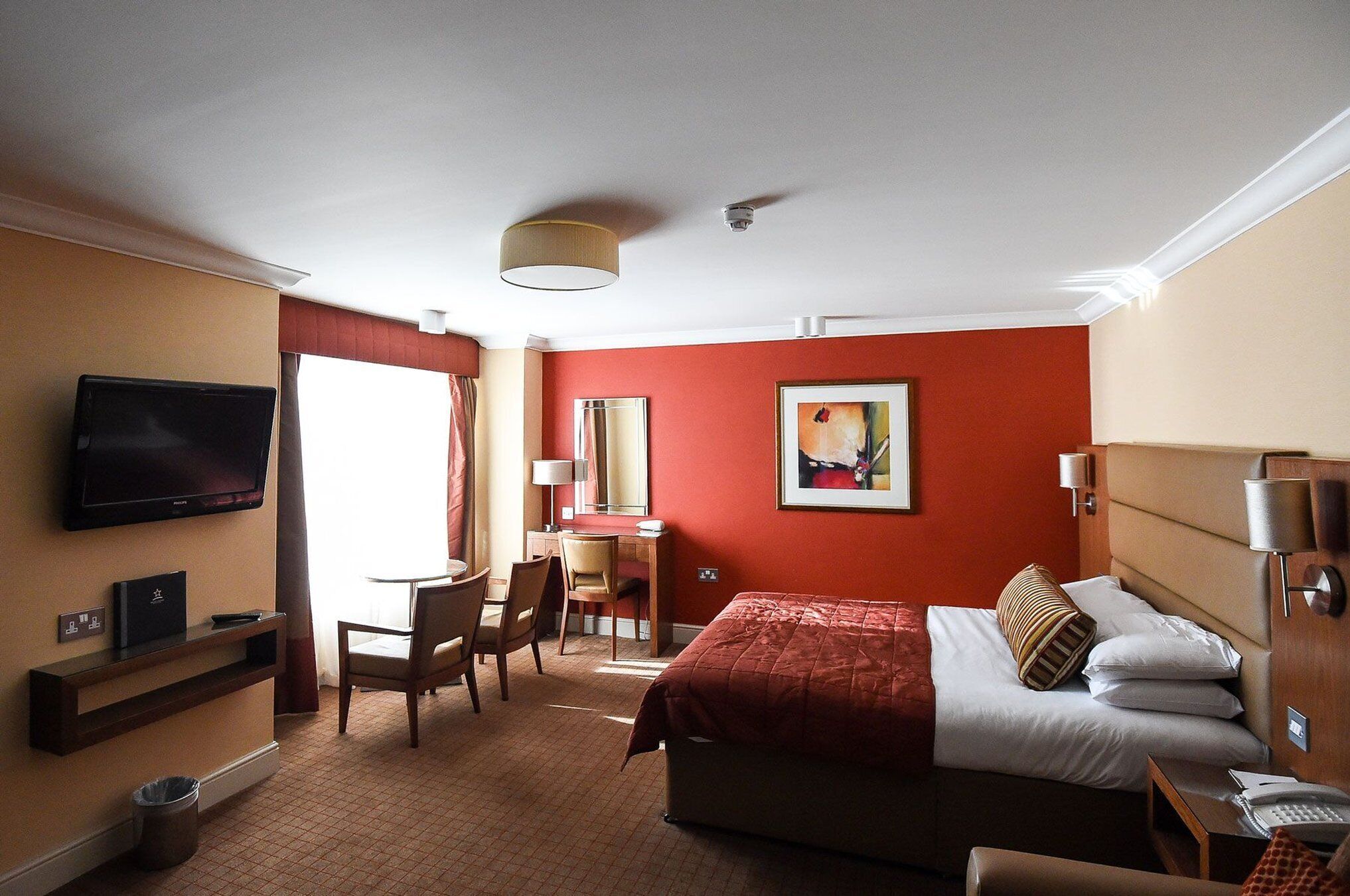 Habitación de hotel con cama, escritorio, silla, televisor y un cuadro en la pared.