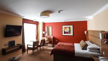 Habitación de hotel con cama, escritorio, silla, televisor y un cuadro en la pared.