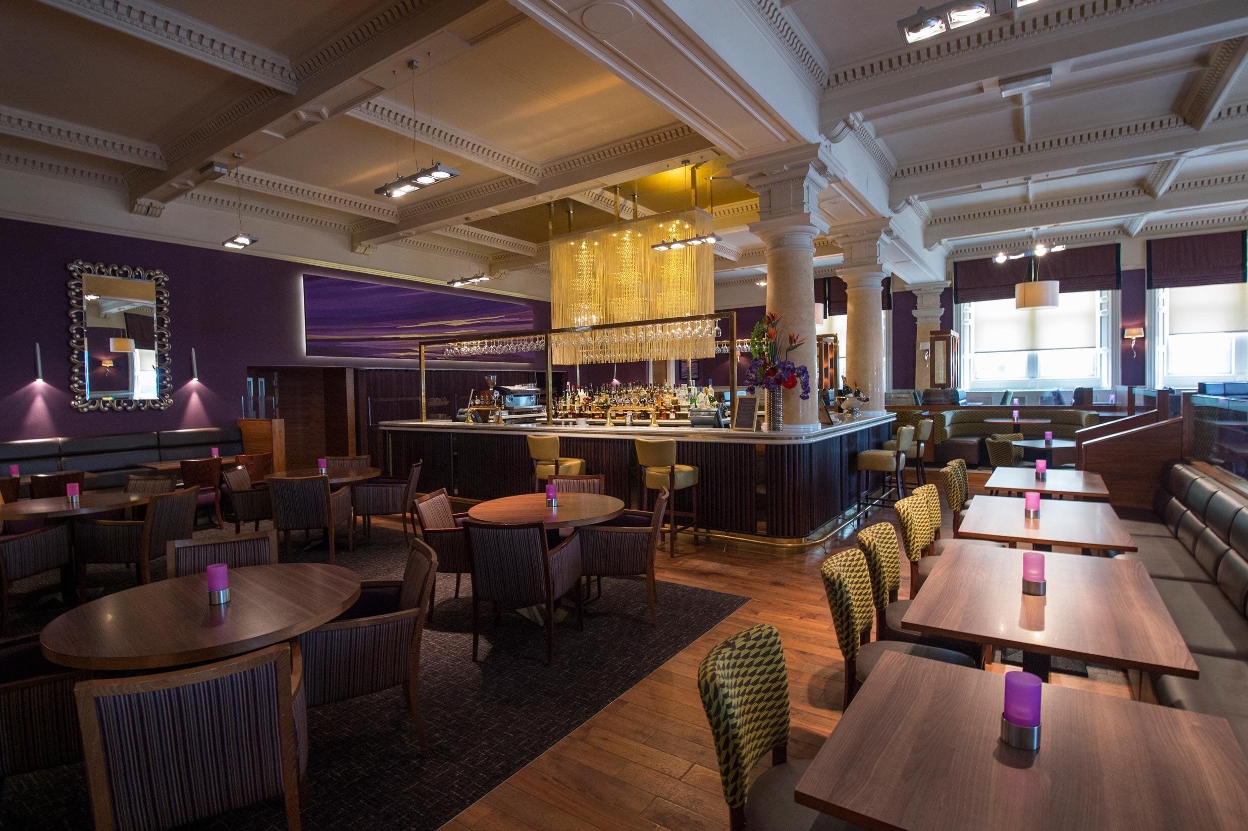 A restaurant with a bar area, multiple seating options including round tables and booths, and a decorative ceiling.