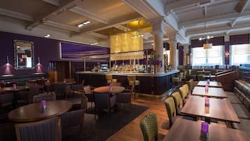 A restaurant with a bar area, multiple seating options including round tables and booths, and a decorative ceiling.