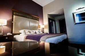 A hotel room with a large bed, a nightstand with a lamp, and a TV mounted on the wall. - Seamill Hydro Hotel & Resort (West Kilbride)