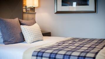 A neatly made bed with a plaid blanket, two pillows, and a wall-mounted lamp.