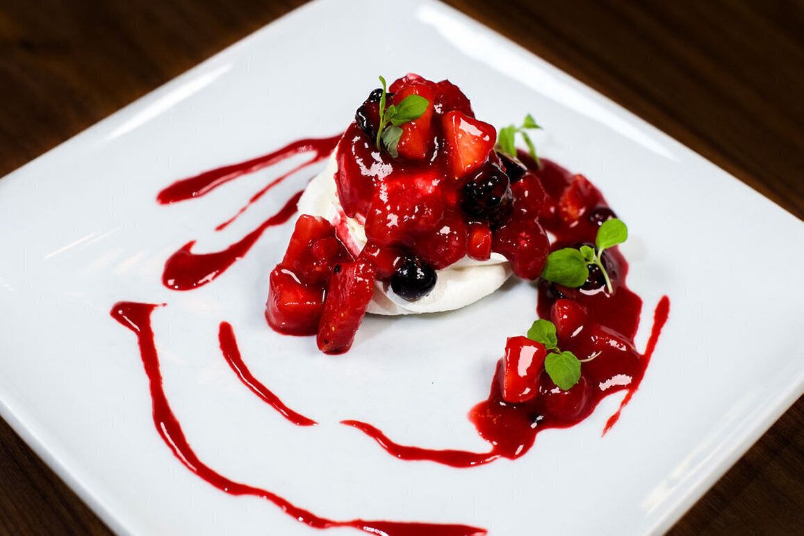 Un postre en un plato blanco con frutos rojos y salsa roja.