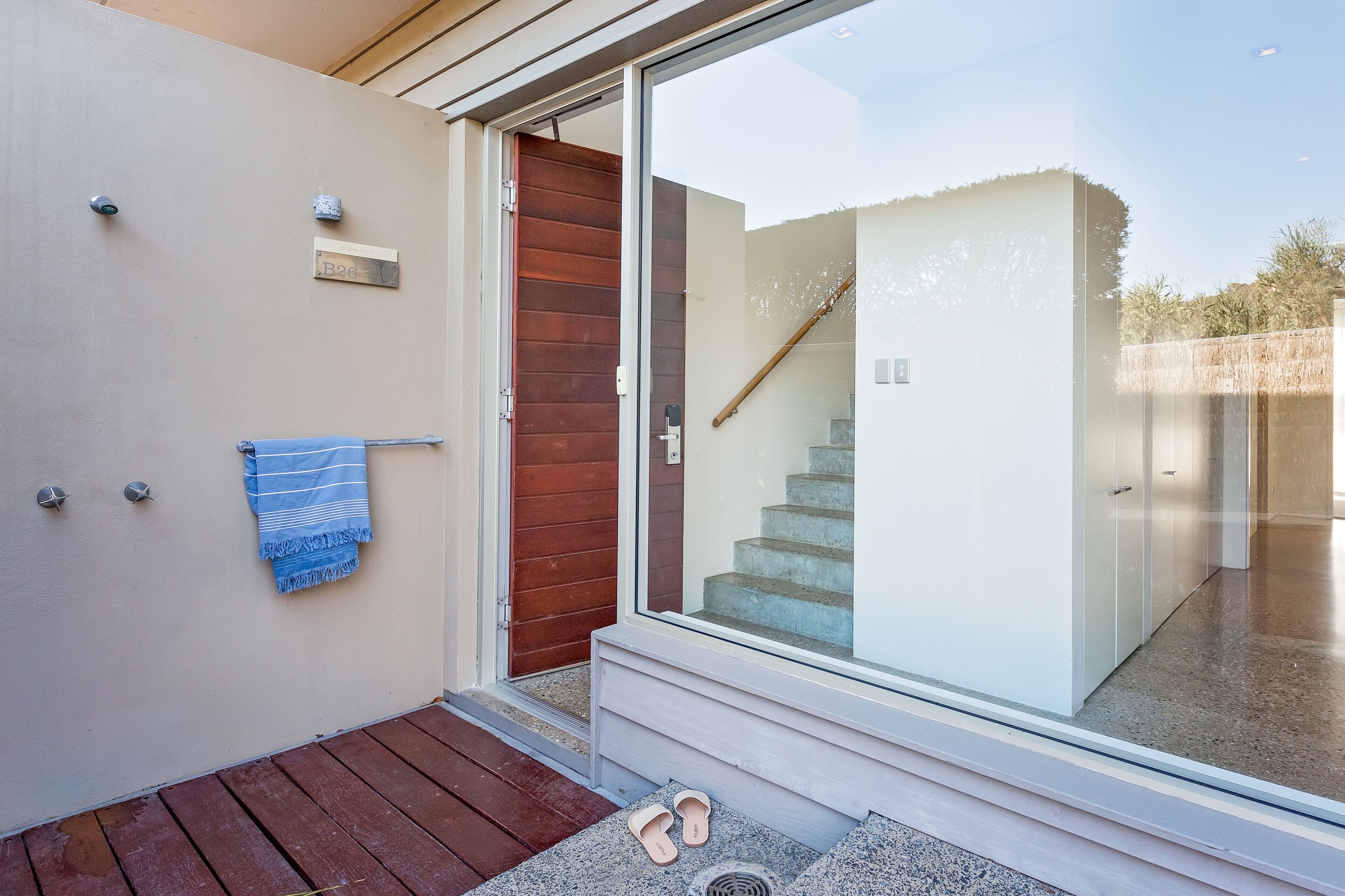 Une entrée moderne avec une porte en verre, une porte en bois et une serviette bleue accrochée au mur.