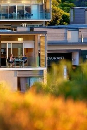A modern building with a glass facade, a restaurant sign, and a dining area with people. - Smiths Beach Resort (Yallingup)