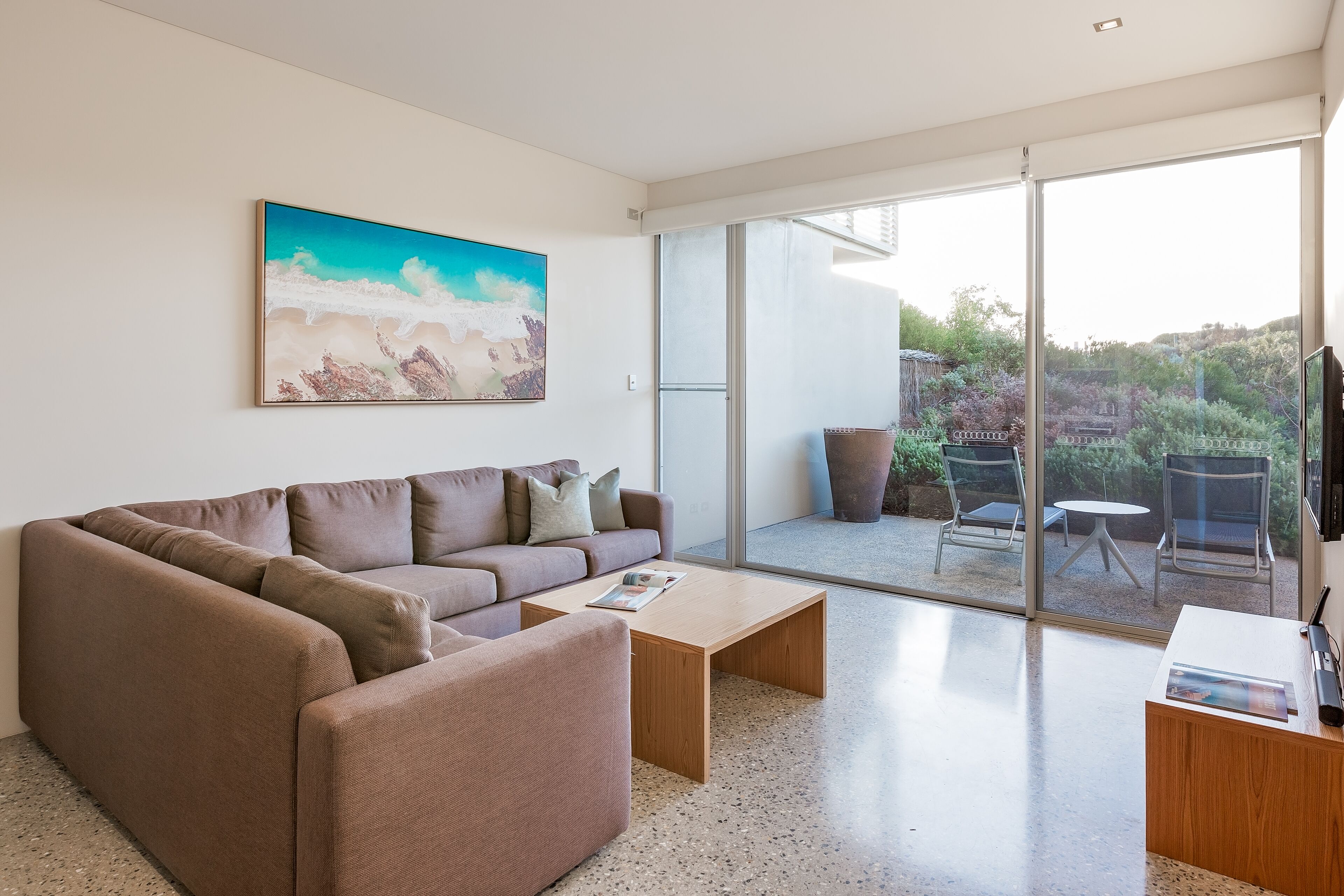 A modern living room with a brown sofa, a coffee table, and a painting on the wall.
