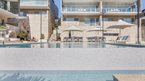 A modern hotel with a large pool, outdoor seating, and a stone facade.