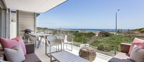 An outdoor seating area with a view of the sea, featuring a table, chairs, and a sofa with patterned cushions.