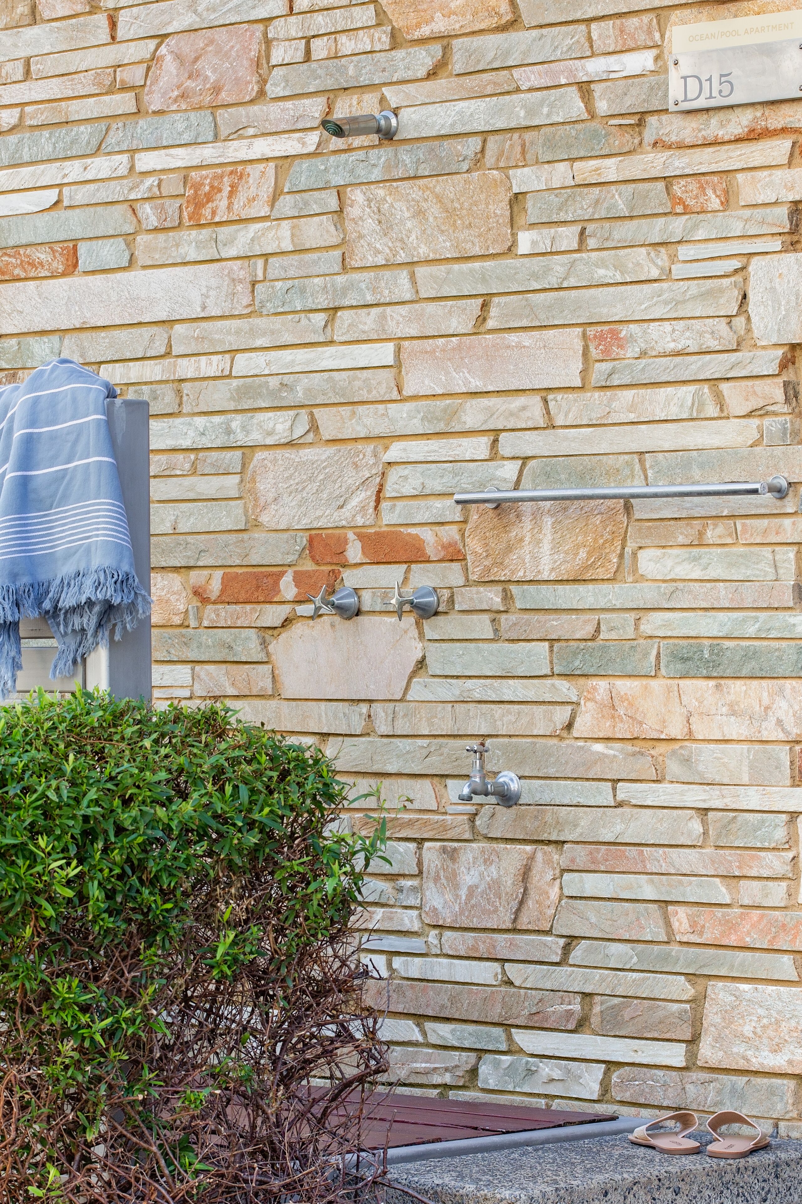 A stone wall with a towel, towel rack, and a pair of sandals.