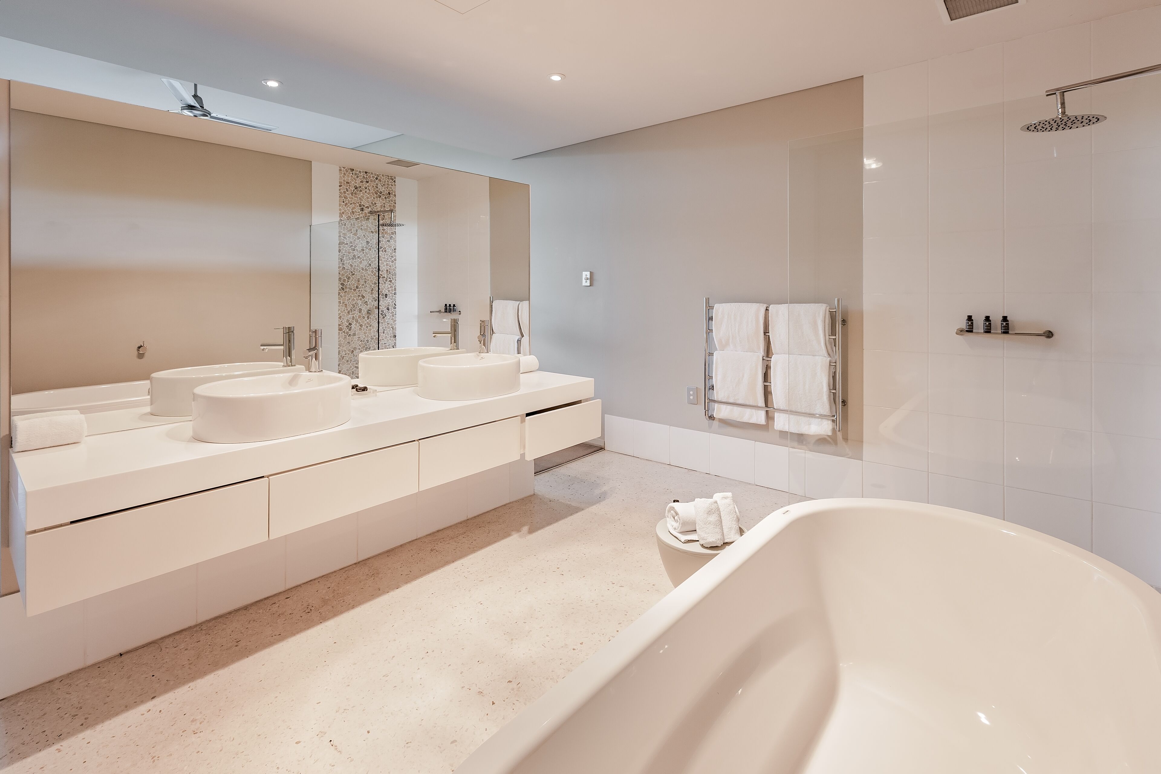 A modern bathroom with a large mirror, two sinks, a bathtub, and a shower.
