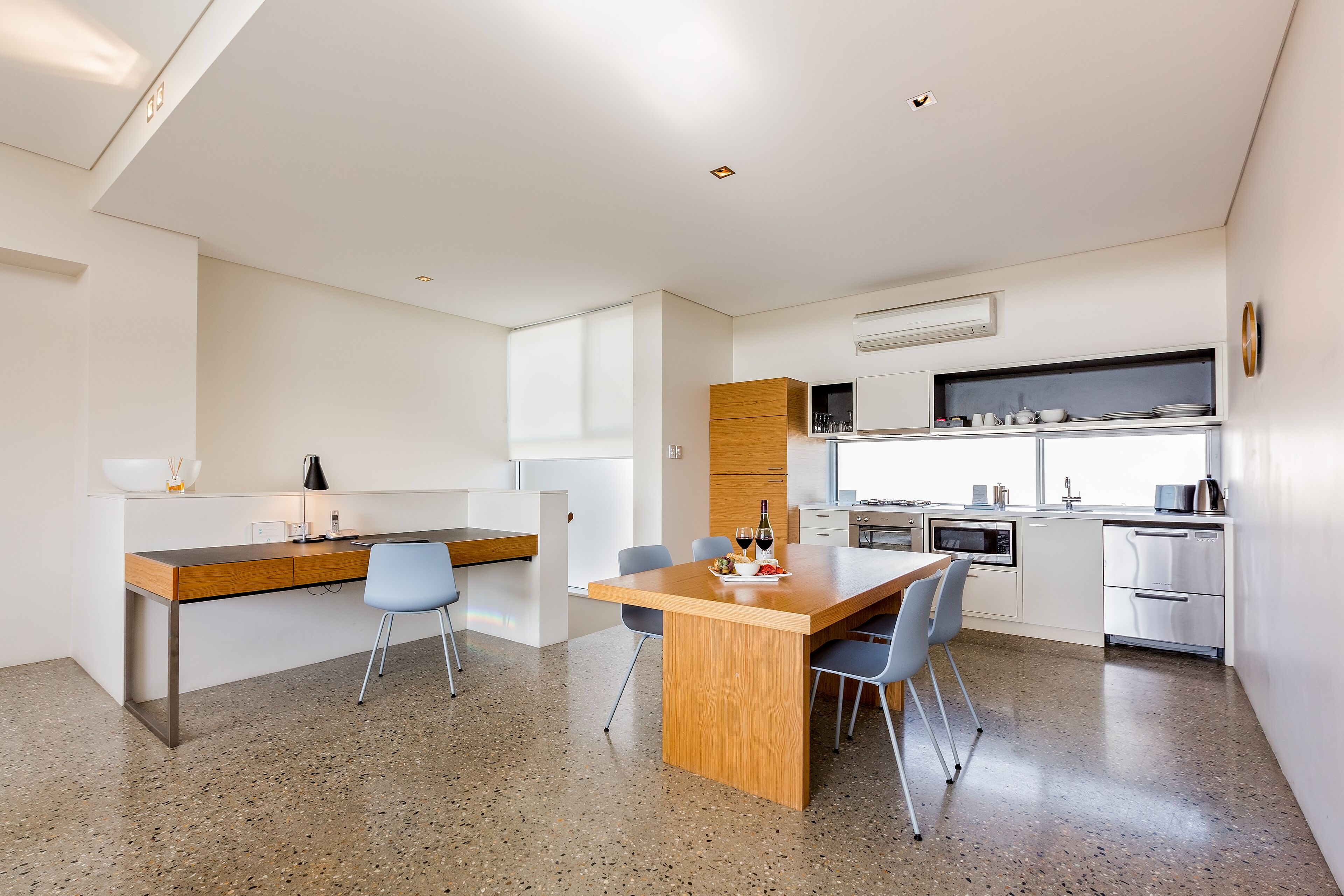 A modern kitchen with white cabinets, a wooden dining table, and a built-in oven.