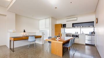 A modern kitchen with white cabinets, a wooden dining table, and a built-in oven.