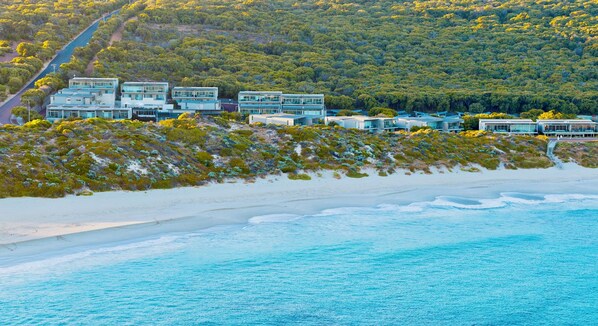 A coastal property with multiple modern buildings, a sandy beach, and a forested hillside. - Smiths Beach Resort (Yallingup)