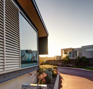 A modern house with a large window reflecting a person relaxing on a couch.