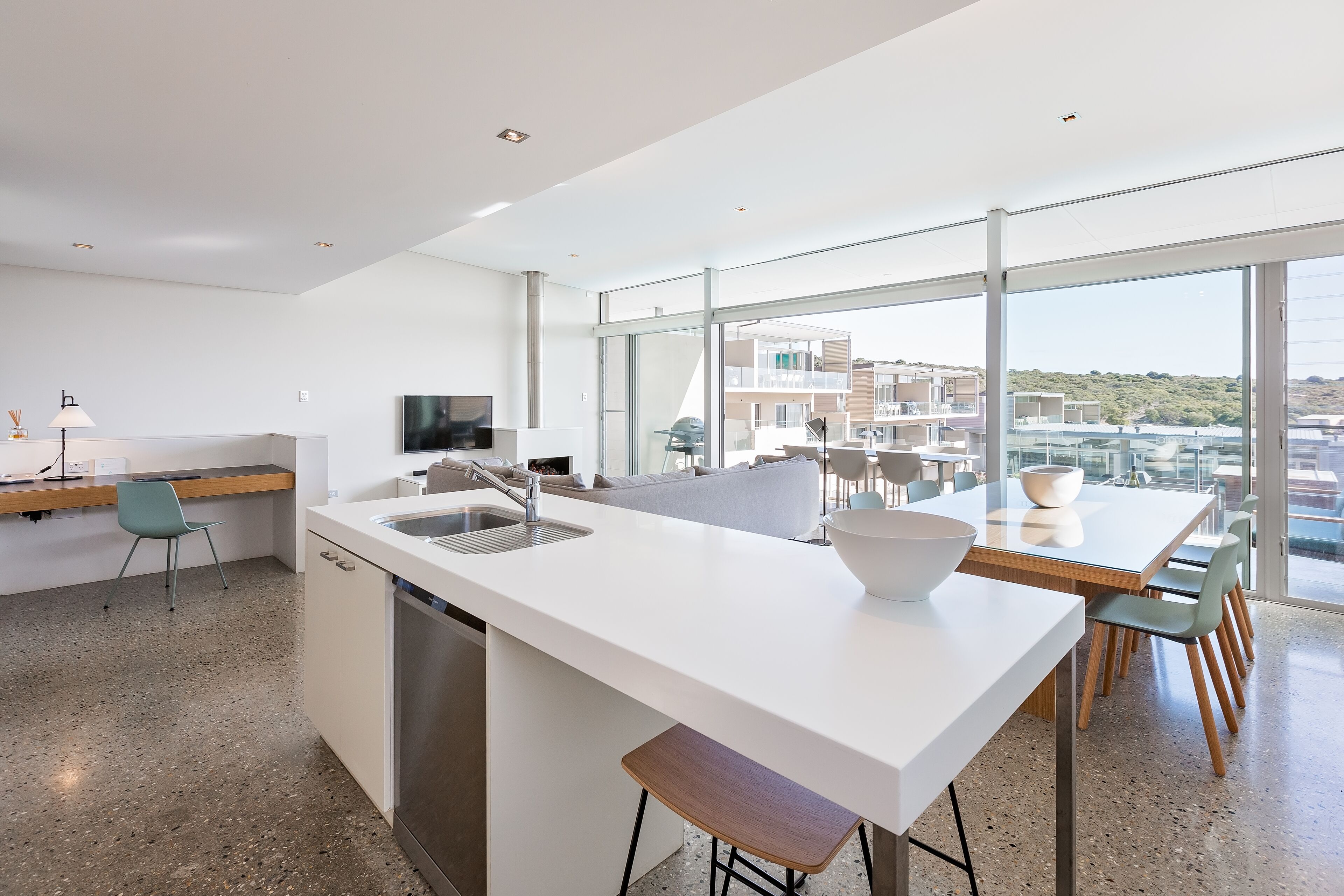 Cozinha moderna com uma ilha grande, área de refeições com mesa de vidro e vista para edifícios através de grandes janelas.