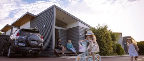 Una casa moderna con un garaje, una camioneta SUV estacionada y un niño montando una bicicleta.