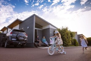 A modern house with a garage, a parked SUV, and a child riding a bicycle.
