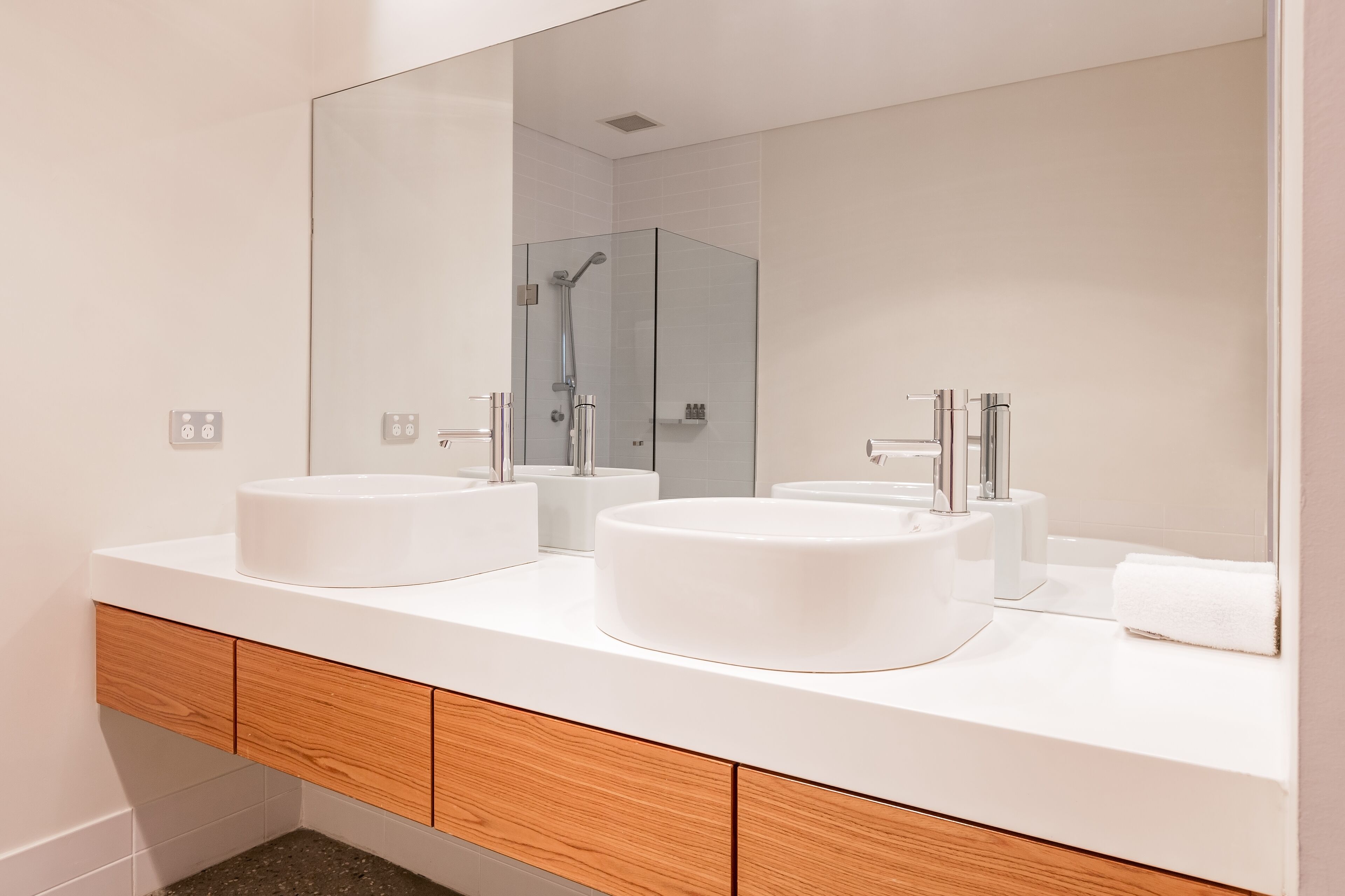 A modern bathroom with two white sinks, a large mirror, and a shower enclosure.
