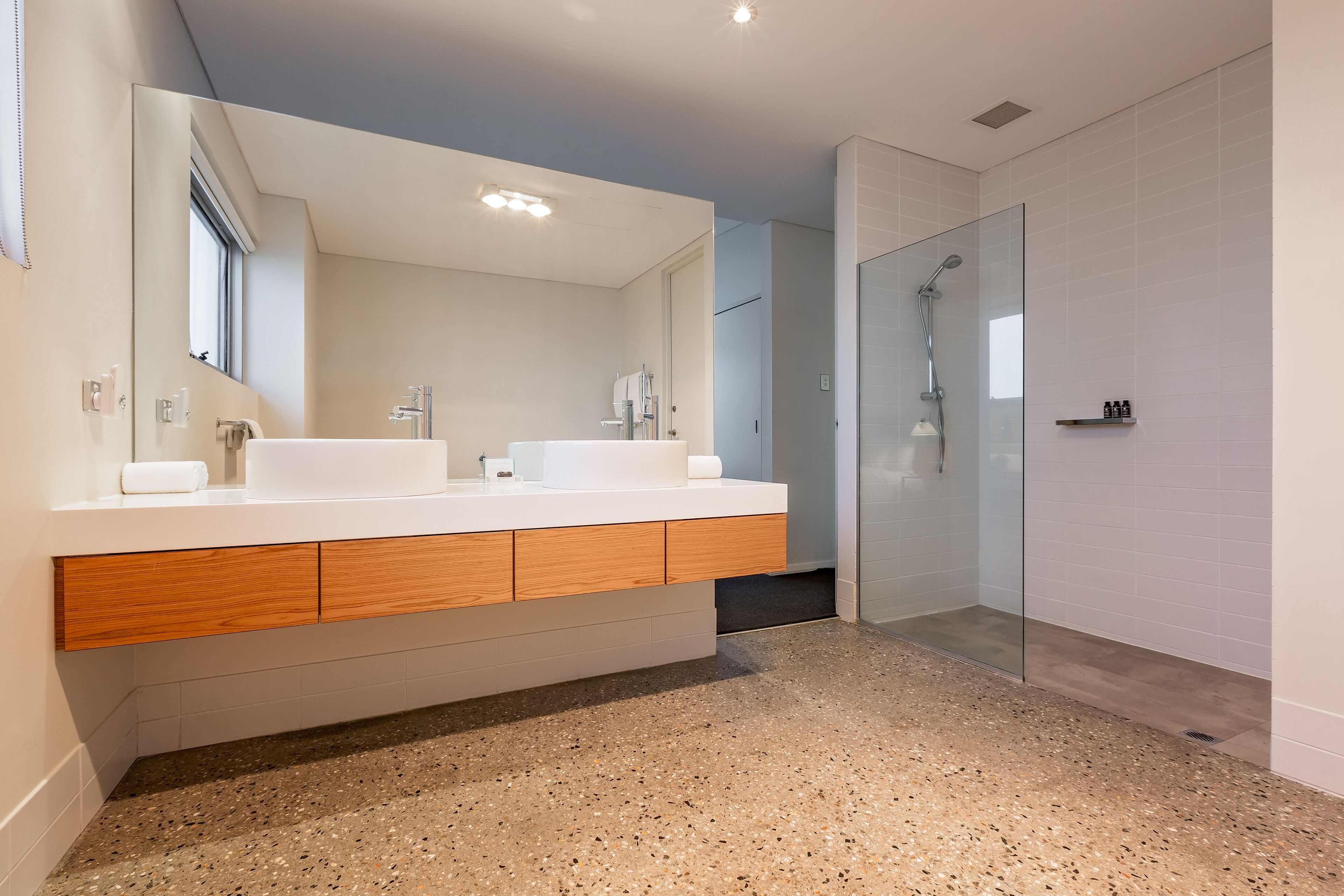 A modern bathroom with a double sink vanity, a glass shower enclosure, and a speckled floor.