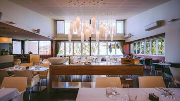 A modern restaurant with a central island, multiple dining tables, and pendant lighting.
