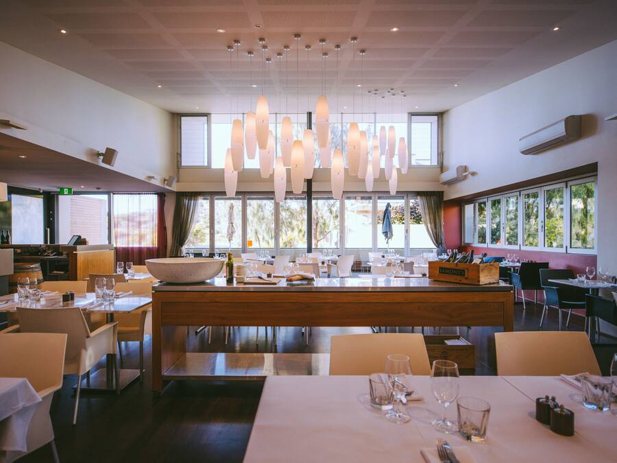 Een modern restaurant met een centraal eiland, verschillende eettafels en hanglampen.