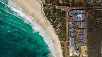 An aerial view of a coastal property with a beach, a parking lot, and a cluster of buildings with a swimming pool.