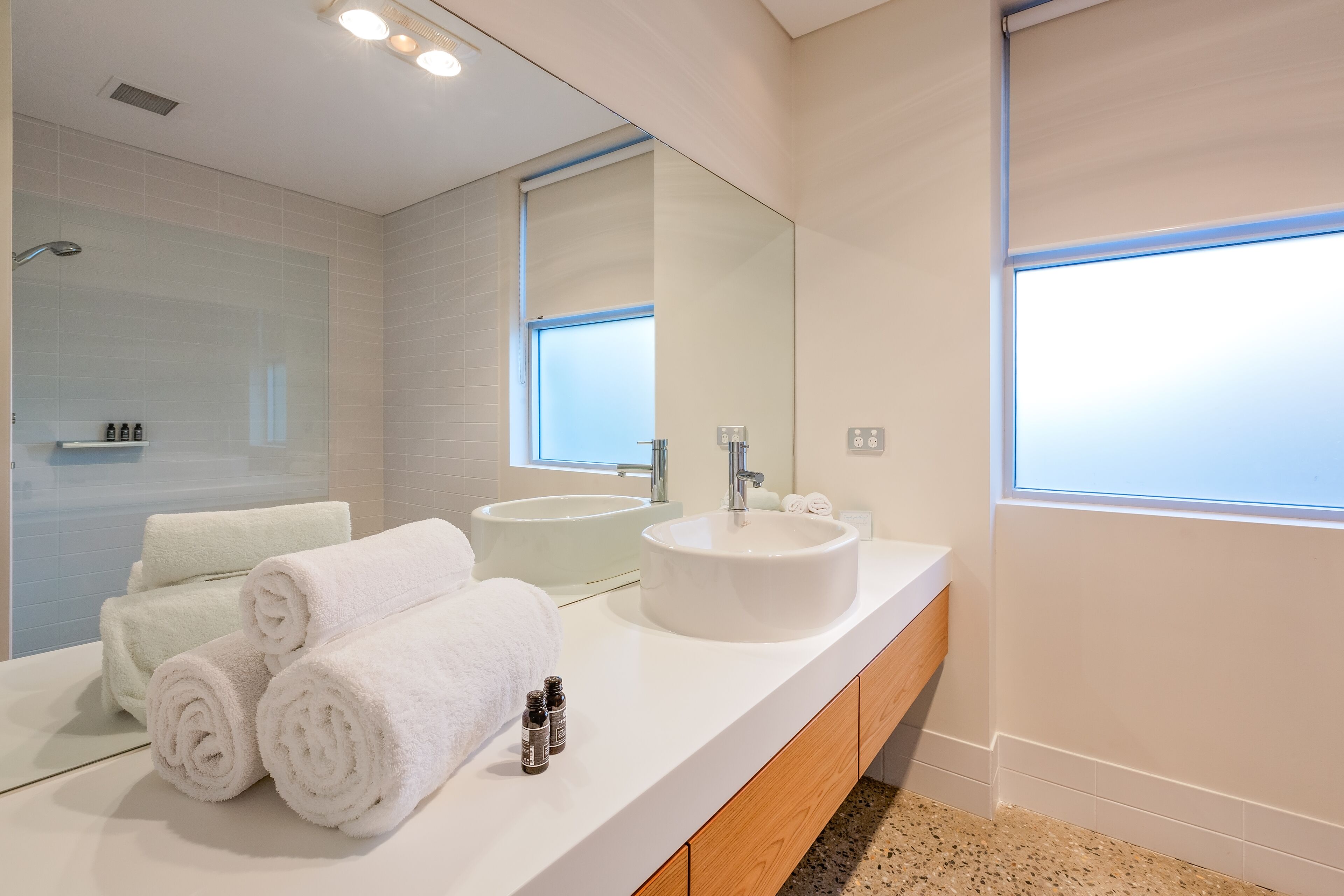 A modern bathroom with two sinks, a large mirror, and a window.
