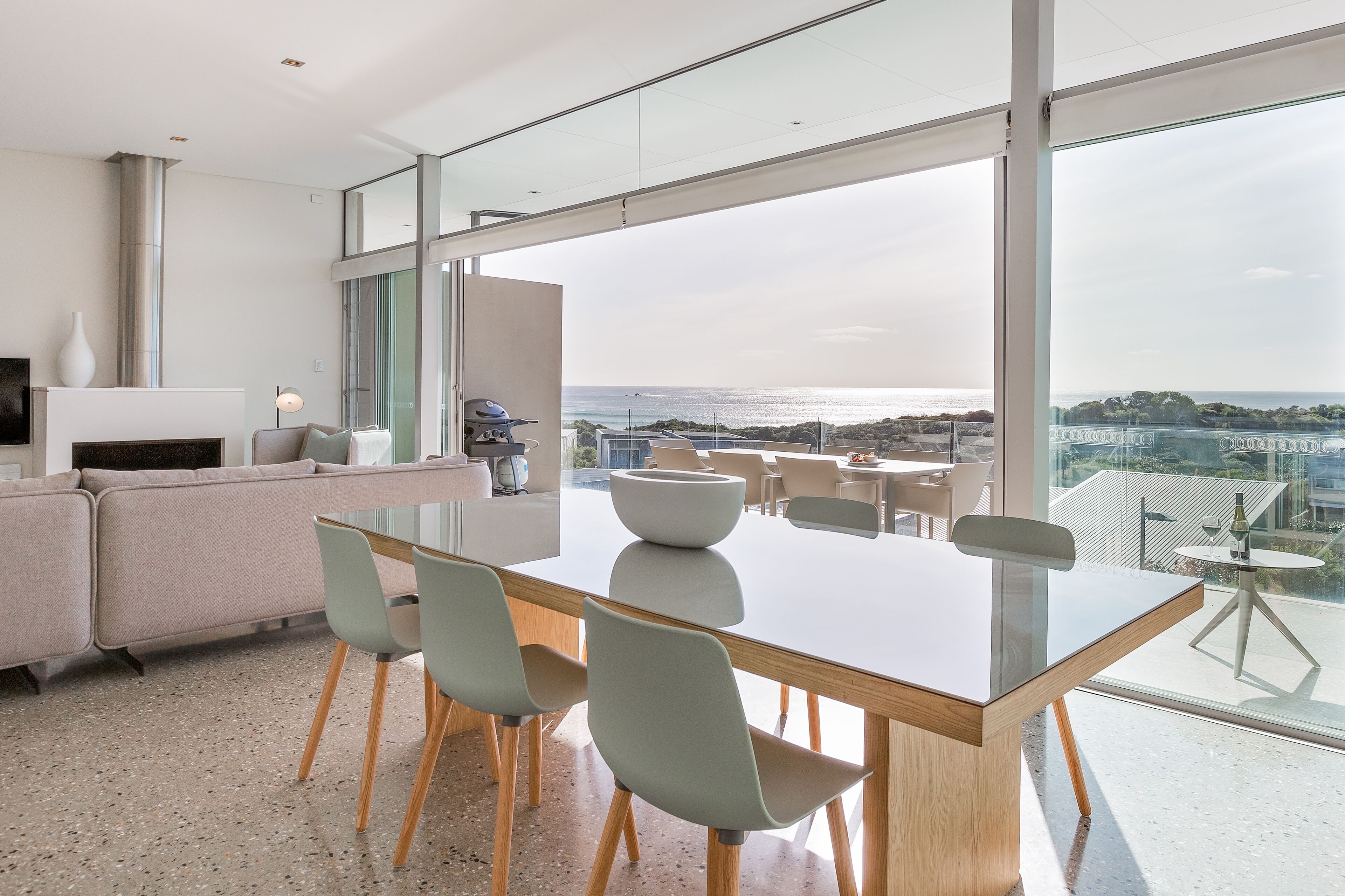 A modern living room with a large glass table, seating, and a fireplace.