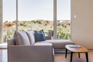 Una sala de estar moderna con un ventanal grande, un sofá y una pequeña mesa de madera.