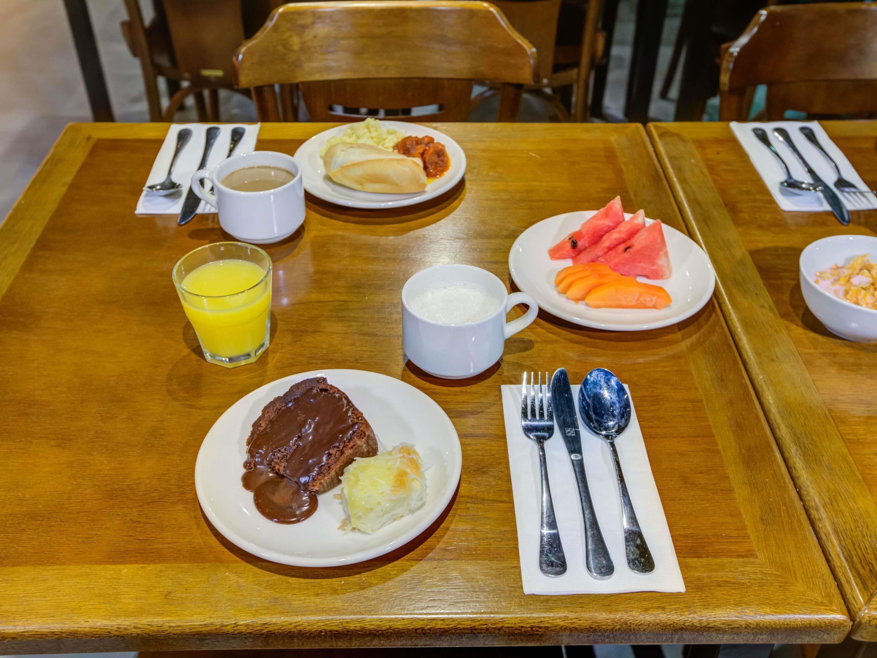 A wooden dining table with plates of food, a glass of orange juice, and a white mug.