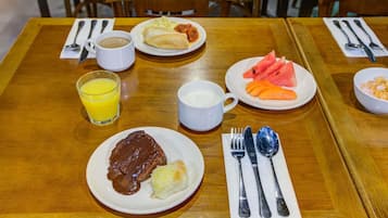A wooden dining table with plates of food, a glass of orange juice, and a white mug.