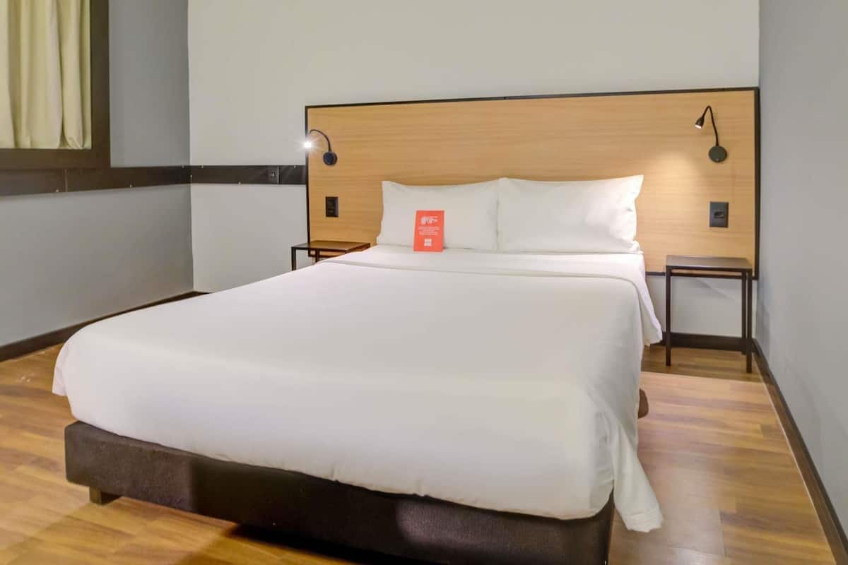 A hotel room with a large bed, a wooden headboard, two bedside tables, and a nightstand.
