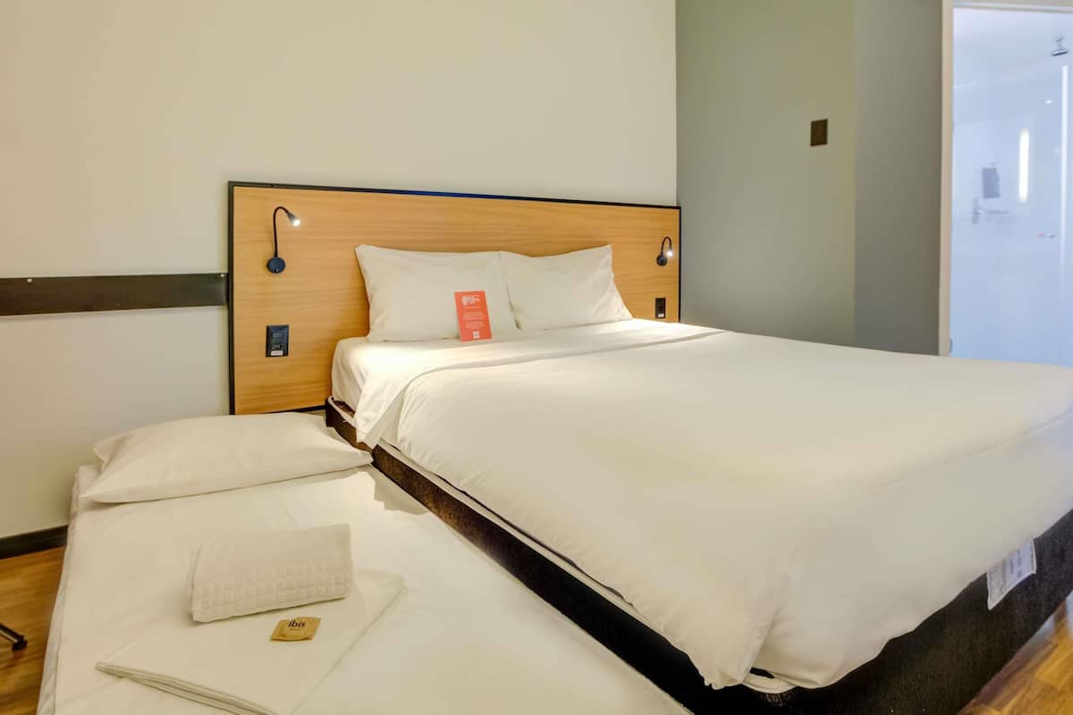 A hotel room with a wooden headboard, white bedding, and a small bedside table with a lamp.
