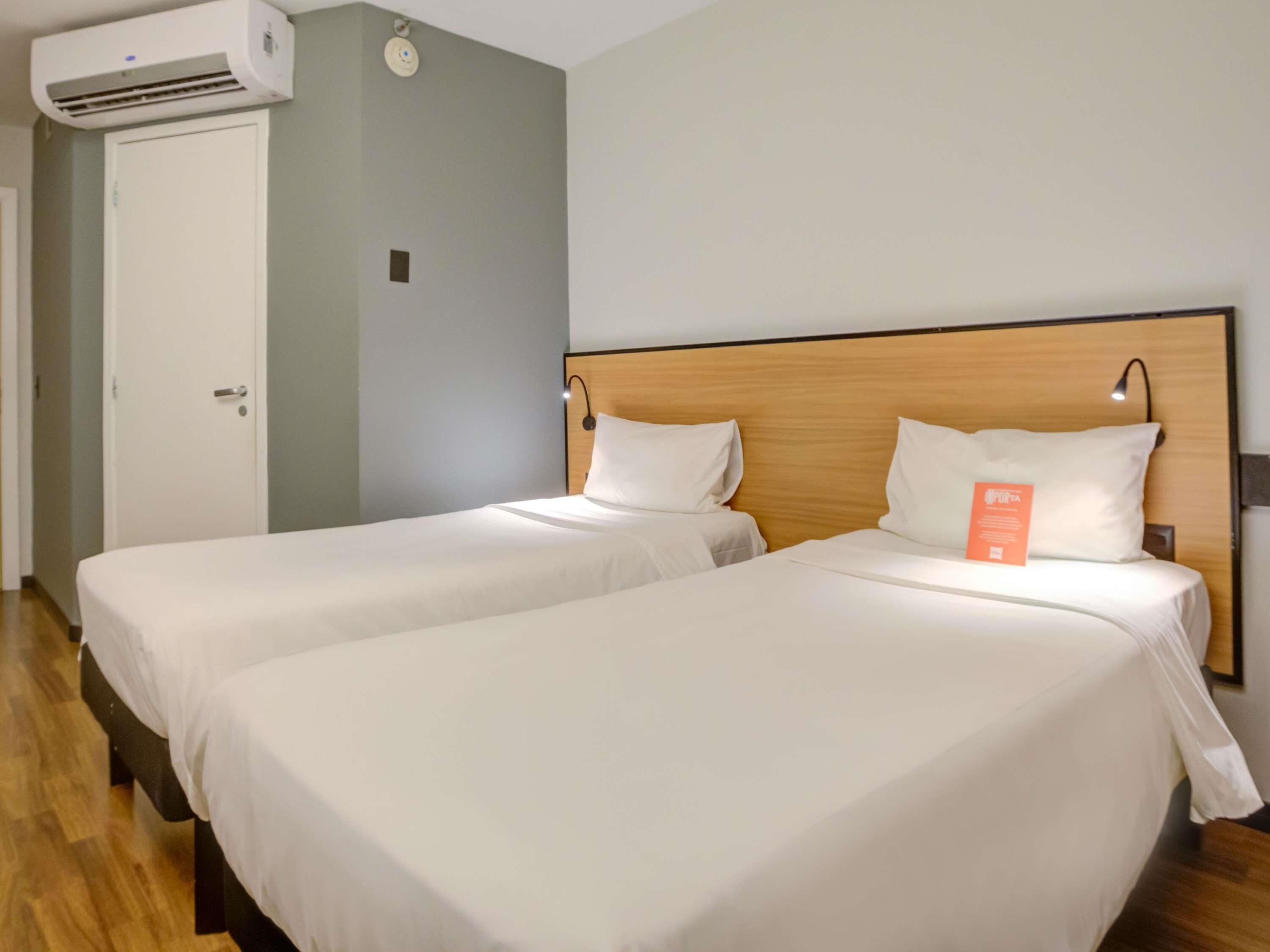 A hotel room with two beds, a wooden headboard, a white wall, and an air conditioning unit.