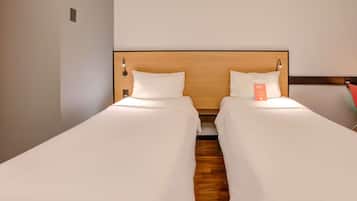 Quarto de hotel com duas camas de solteiro, cabeceiras de madeira e uma pequena placa laranja na cama à direita.
