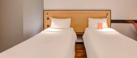 A hotel room with two single beds, wooden headboards, and a small orange sign on the right bed.
